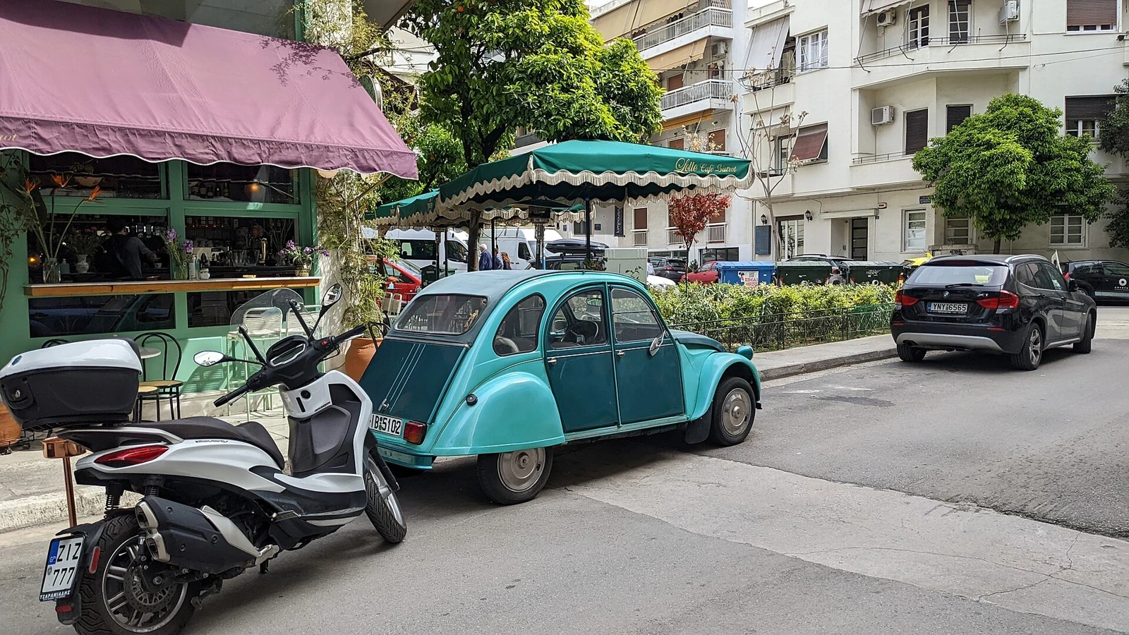 Uliczna kawiarnia pod markizami, turkusowy Citroën i budynki z balkonami w Atenach