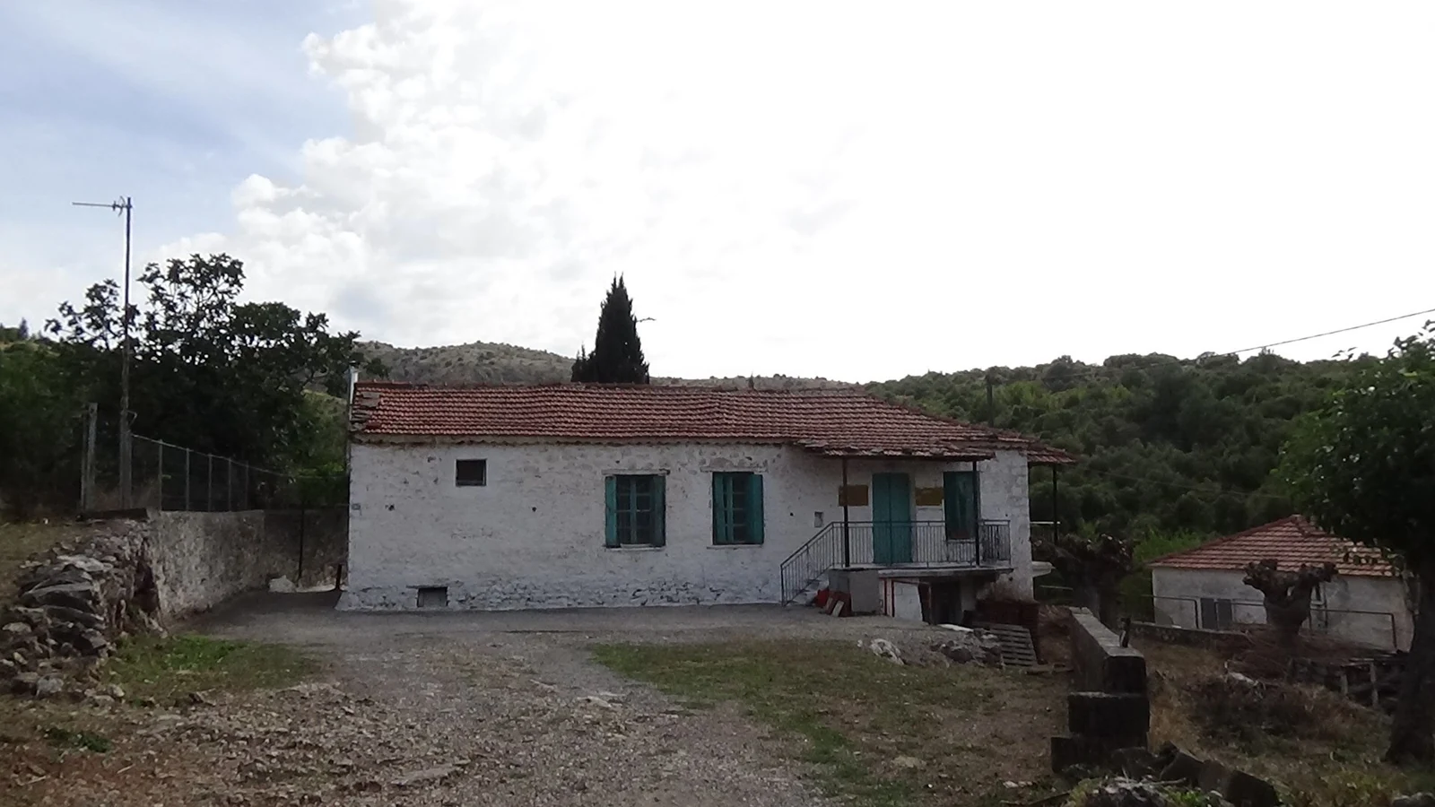 Bielony kamienny dom z zielonymi okiennicami, dachówką i schodami we wsi Mavriki w Arkadii