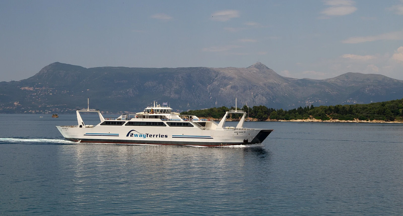 Biały prom z oznaczeniem 2wayferries płynący po wodzie w okolicy Korfu, z górzystym wybrzeżem w tle