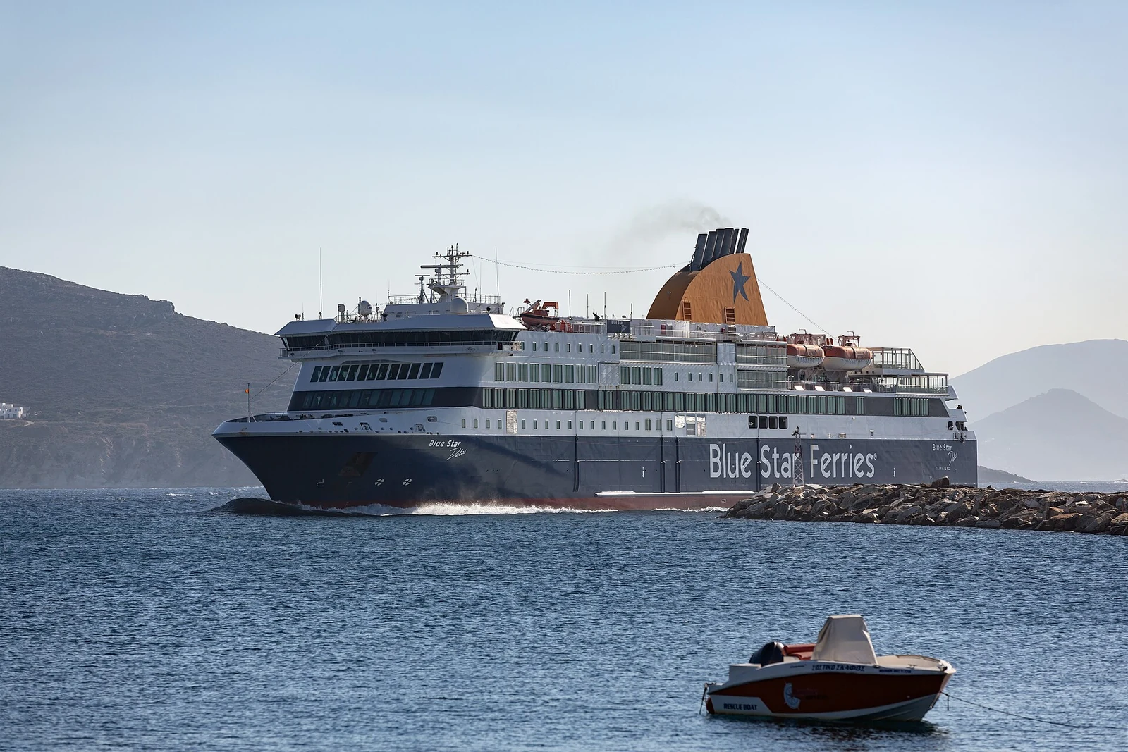 Prom Blue Star Delos przy falochronie portu Chora na Naksos, z małą łodzią na pierwszym planie