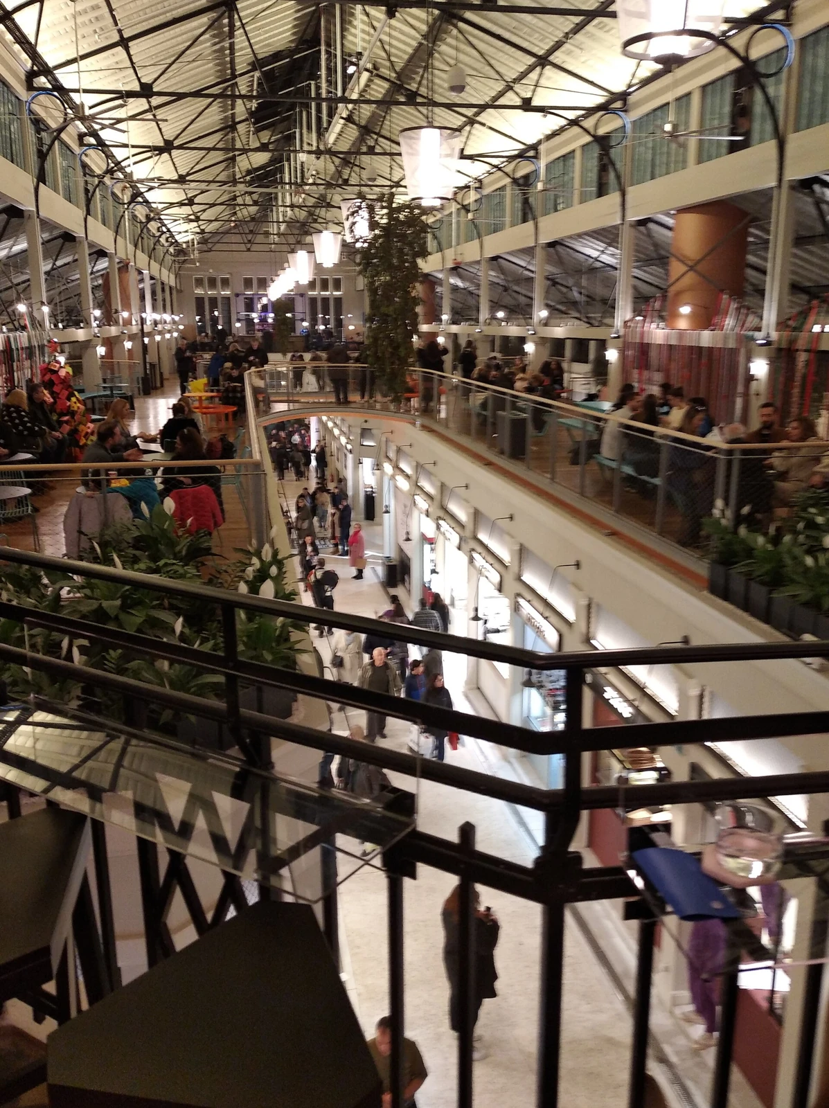 Wnętrze hali Agora Modiano w Salonikach z galerią, stolikami i przechodniami pod stalową konstrukcją dachu