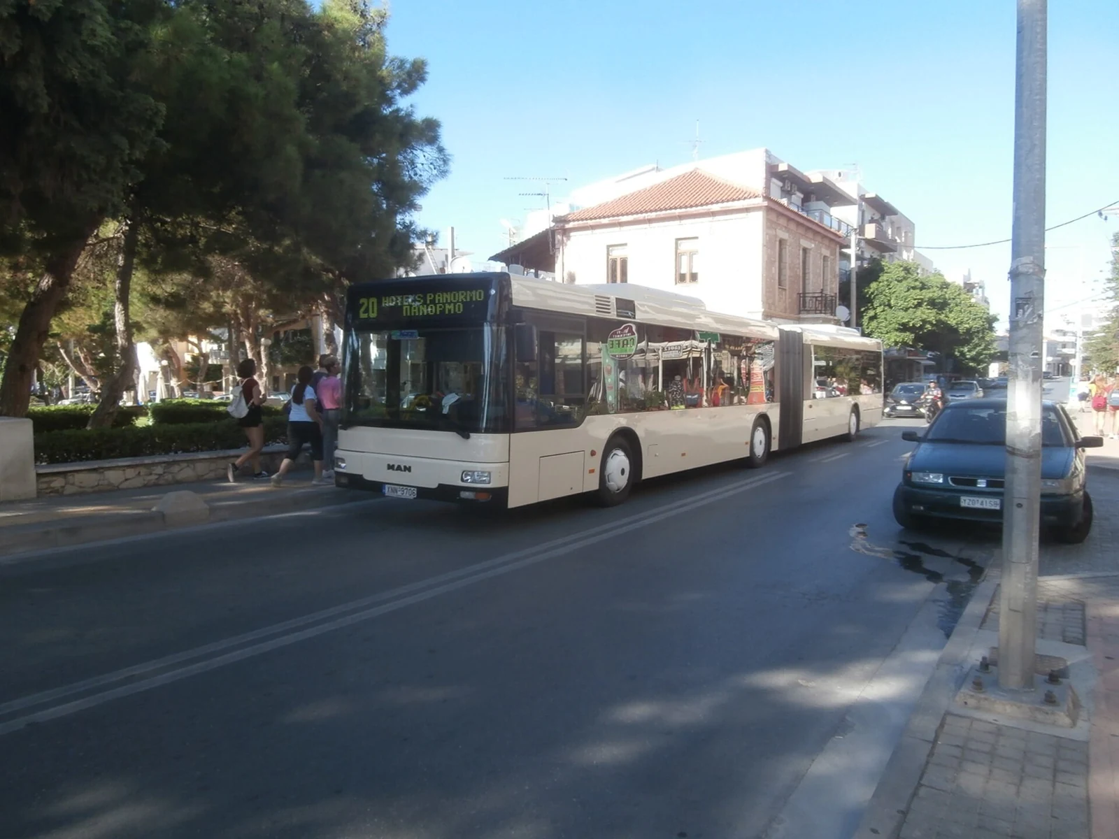 Przegubowy autobus MAN na ulicy w Rethymno, z budynkami, drzewami i zaparkowanymi samochodami w otoczeniu